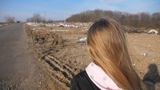 一头金发的小女孩在乡下很多垃圾附近的车道上行走图片