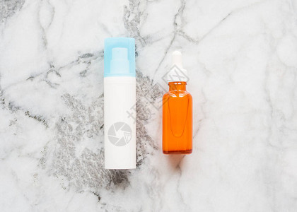白色泵分配器中的面霜和大理石板上橙色玻璃瓶中的皮肤血清图片