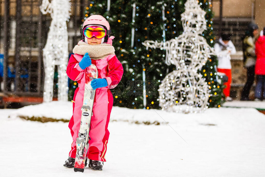 寒假时戴着护目镜和头盔的小女孩在户外拿着滑雪板图片