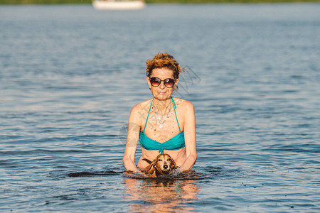 有魅力的成熟女人喜欢在夏天玩她的狗夏季时间和生活方式腊肠犬在河里游泳一位老妇人帮助她的小图片