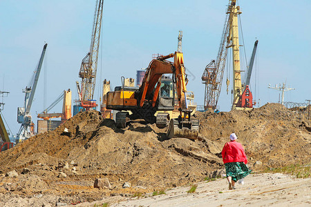 在一大堆沙子上的挖掘机和远处建筑工地的建筑机械图片