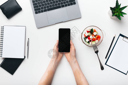 使用带空白屏幕的智能手机在工作场所享受健康午餐的妇女图片