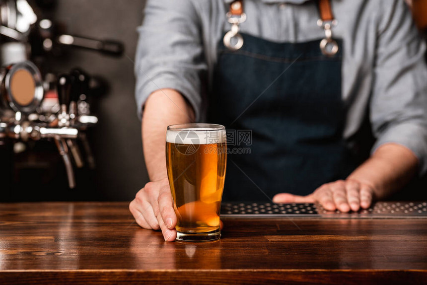 在酒吧发行啤酒围裙酒保在酒吧内部的木柜台上给客户一杯图片