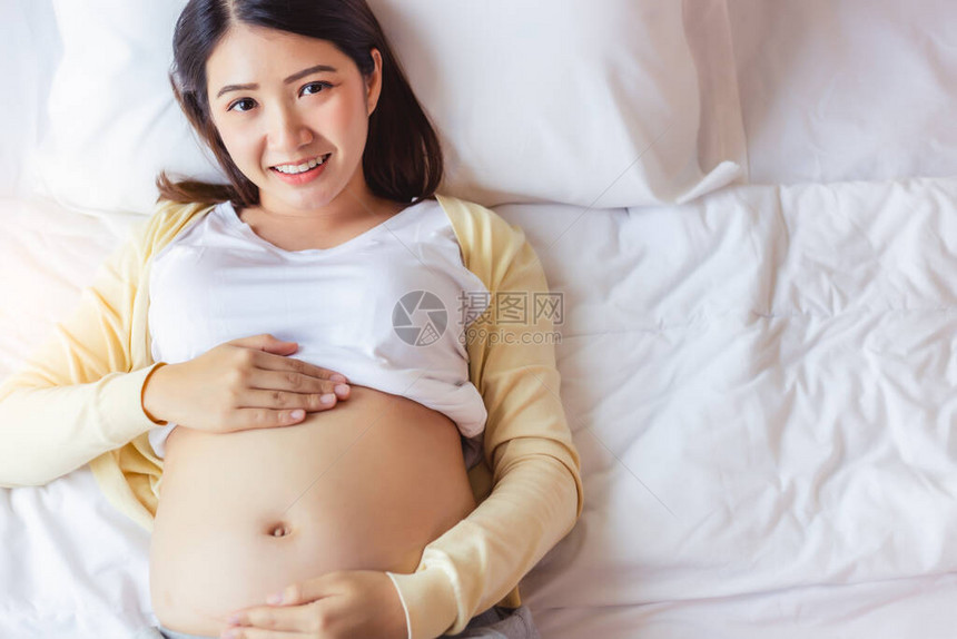 快乐的怀孕年轻亚洲女人抚摸着肚子图片