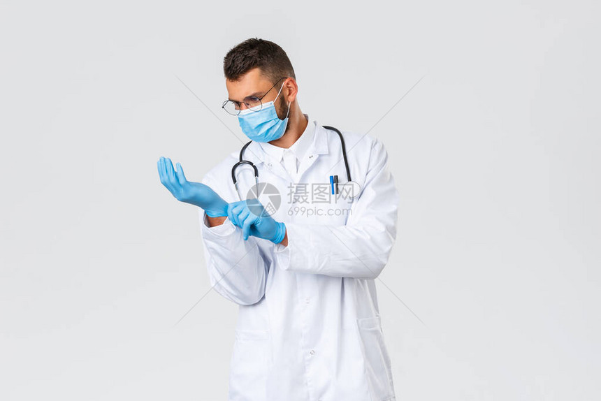 身穿白色磨砂和医用口罩的年轻医生戴上橡胶手套图片