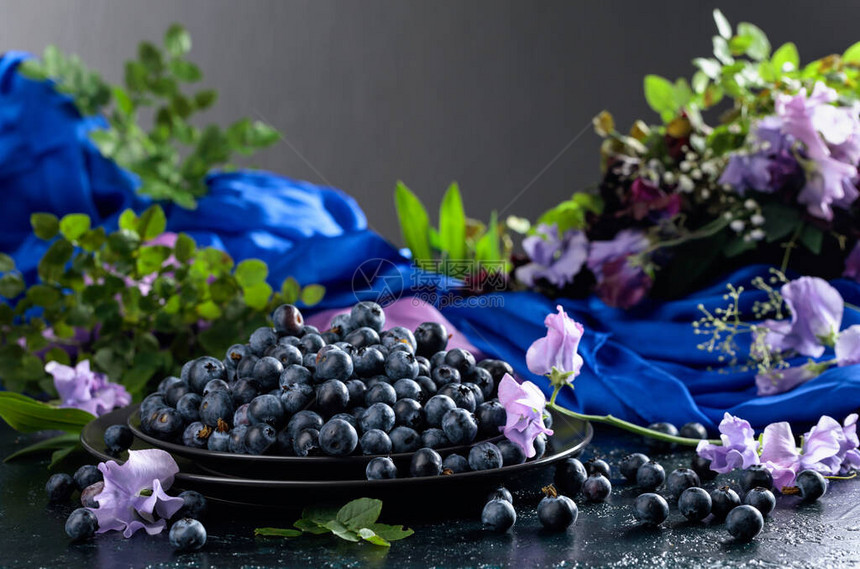 黑板上的新鲜多汁的蓝莓夏季静物与蓝莓彩色甜豌豆和草甸图片