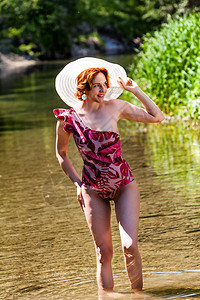 戴着太阳帽的红头发年轻女人穿着泳衣站在海滩上的水图片