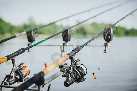 在湖或河上钓鱼的年轻渔夫钓鱼期间装备齐全的三根鱼竿的图片旁边没有人卷轴和引诱阳背景图片