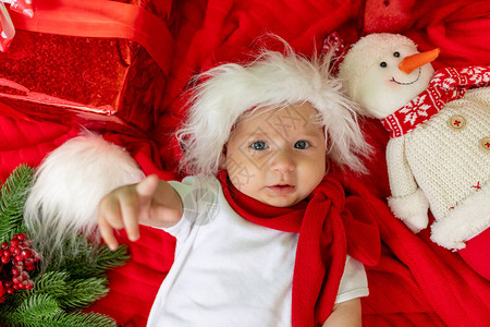 一个戴着圣诞帽的孩子躺在红色背景的礼物中图片