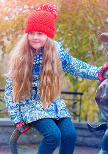 一个穿着蓝色夹克和一顶红色帽子的小可爱顽皮女孩在圣诞节假期的冬天在外面玩耍背景图片