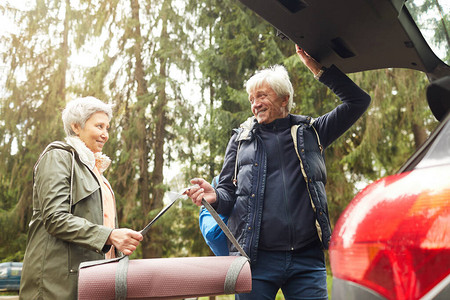 低角度的现代高龄夫妇在森林中漫步时打开汽车后备箱并快乐笑图片
