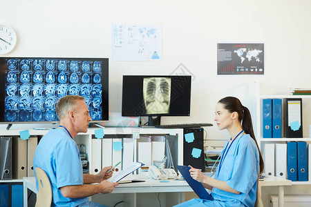 两名成年医生坐在现代诊所内部工作场所时说话时交谈的侧面照片图片