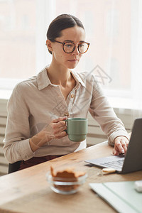 在舒适的家庭办公室工作场所使用膝上型电脑时戴眼镜的优雅女商人图片