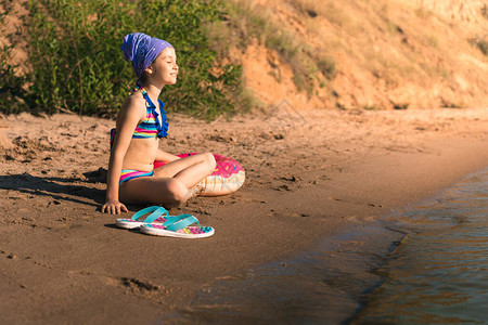 一个穿着泳衣的小女孩坐在海边沙滩上的充气圈旁边图片