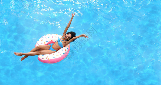 兴奋的年轻女子享受夏日阳光在泳池风景上方的充气环上图片