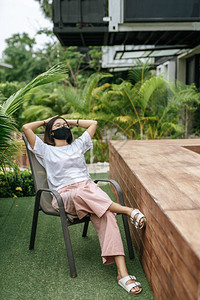 戴面罩的妇女坐在花园游泳池旁边的椅子图片