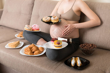 饥饿的孕妇坐在沙发上的特写是吃很多不健康的食物图片