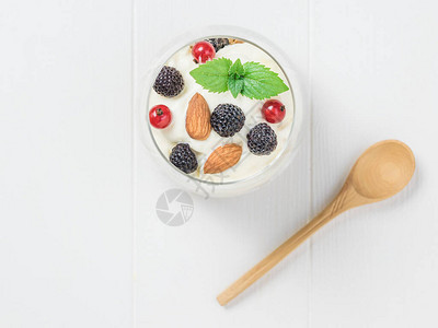 白木桌上的木勺和一杯酸奶面粉和浆果图片