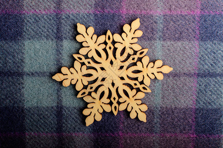 浅蓝色和灰色纹理纺织羊毛材料背景上的一片精致的浅棕色木质雪花图片
