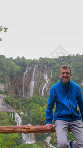 一个年轻人靠在木栏杆上在十六湖公园的背景瀑布中身穿蓝色连帽衫的少图片