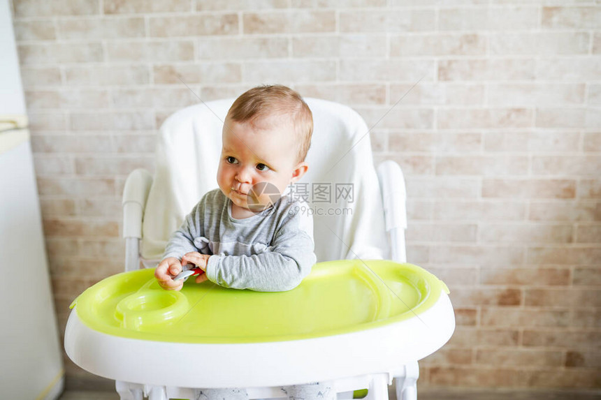 婴儿用勺子自己吃食物孩子在阳光明媚的厨房高脚椅背图片
