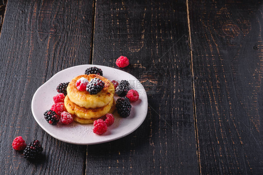 小屋奶酪煎饼和糖粉凝乳油条甜点覆盆子和黑莓浆果放在盘子里图片