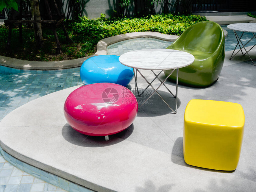 现代明亮的颜色椅子和室外游泳池旁边的各种形状和圆桌游泳池和绿色花园附近空荡的图片