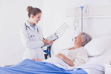 医生或护士在医院的病房巡诊期间与一位高级女病人交谈图片