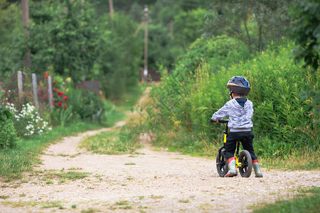 小男孩在农村骑着带头盔的平衡车没有踏板的自行车后视图夏季户外活动图片