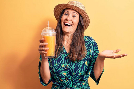穿着暑假帽子的年轻美丽的黑发美女喝着一杯橙汁欢庆成就笑得开心图片