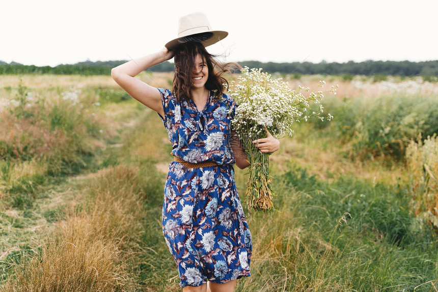 穿着蓝色复古连衣裙和帽子的年轻女子在草地上与白色野花共舞图片