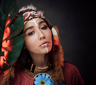身着传统羽毛帽和衣服的漂亮年轻美国印第安女人拿着一片绿色的热带大叶图片