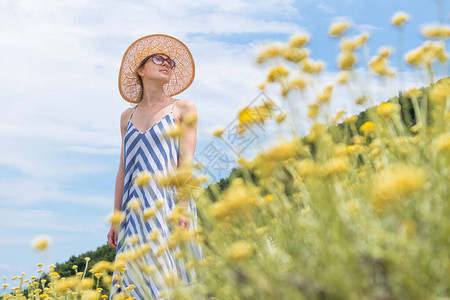穿着条纹夏装和草帽的年轻女子站在超级盛开的野花中图片