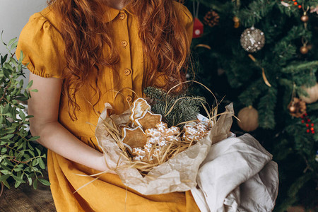 一个穿麻布裙的红发女孩在圣诞树的背景下把一盒姜饼放图片