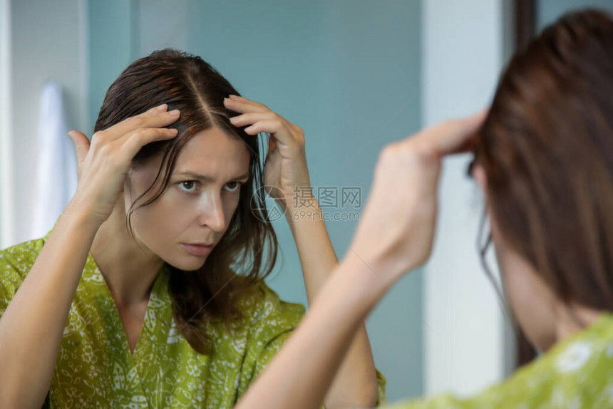 一位漂亮年轻女子在镜子前检查头皮和头发根颜色白发脱发或头皮干图片