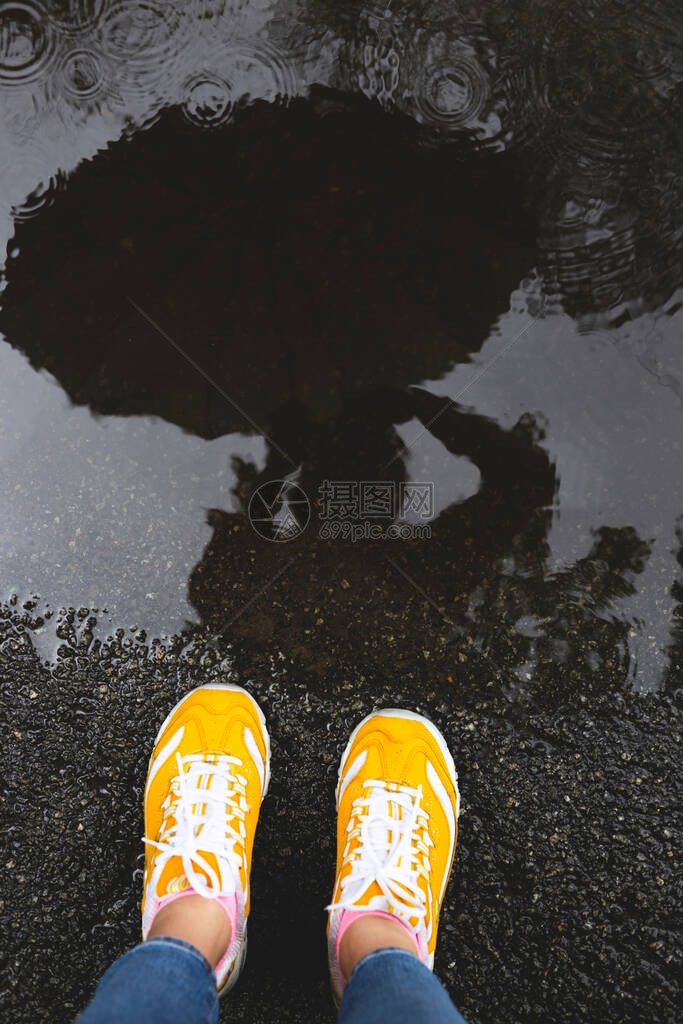 有雨伞的女子在水坑中出现青蓝黄色运动鞋和图片