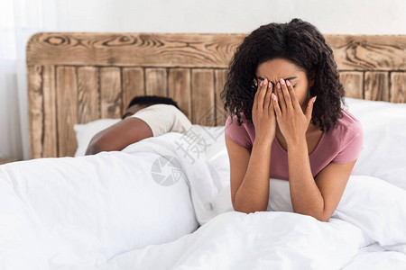 坐在睡梦中男人旁边的床上哭泣的非裔美国女人图片