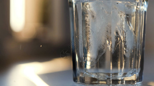 在模糊的背景上将水倒入玻璃杯中的特写将清水倒入装有冰块的空图片
