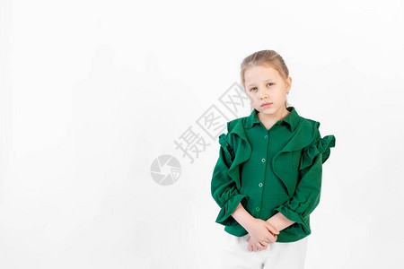 一个810岁悲伤的女孩站在绿色衣服的白色孤立背景上写图片