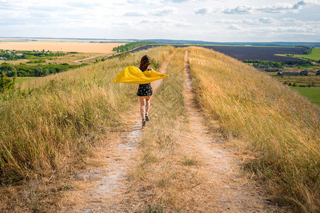 一个穿裙子的女孩和在风中飘扬的黄色斗篷沿着图片