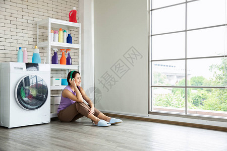年轻的亚洲女人坐在洗衣机旁边图片