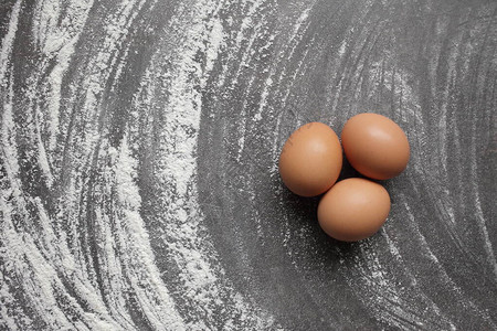 三个鸡蛋和面粉灰色背景表上鸡蛋和面粉用于烘焙产品的产品图片