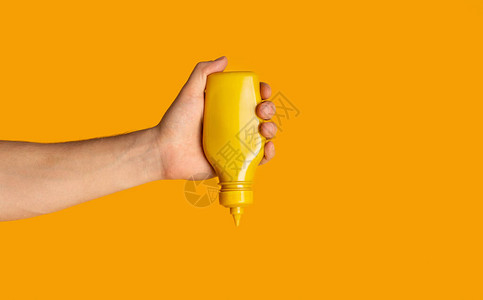 男用手挤压瓶子橙色背景上加芥末关图片