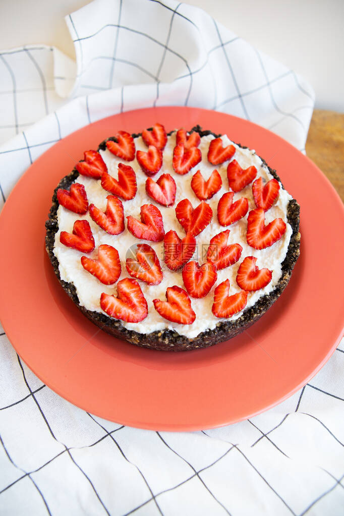 用心形草莓装饰的草莓芝士蛋糕放在珊瑚色的盘子上图片