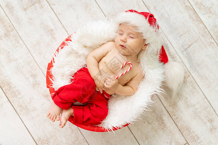 一个穿着圣诞老人服装的熟睡的孩子躺在浅色木质背景上图片