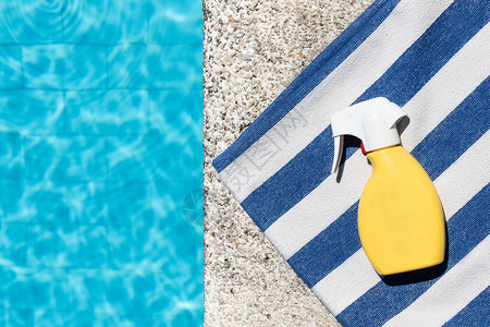 在游泳池边缘的一条蓝色和白色条纹毛巾上喷洒阳光屏幕复制空图片