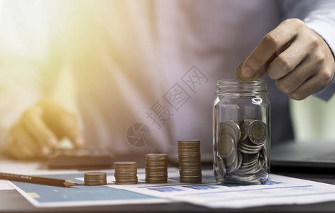 商人用硬币来储蓄罐子和使用计算器为了金融会计投资概念而节省资金图片