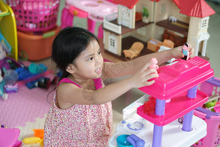 亚洲儿童可爱或小女孩微笑和思考玩厨房玩具图片