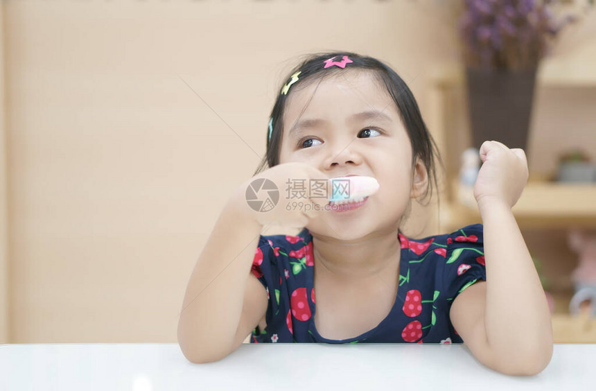 亚洲儿童可爱的过敏牙齿或小女孩在儿童牙科诊所或幼儿园教室和学前托儿所享受美味的草莓冰淇图片