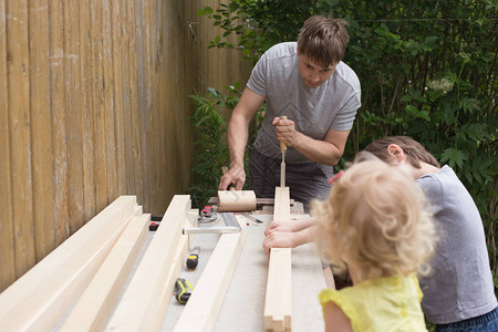 两个孩子在乡间别墅后院协助父亲进行DIY活动男人正在使用凿子工作图片